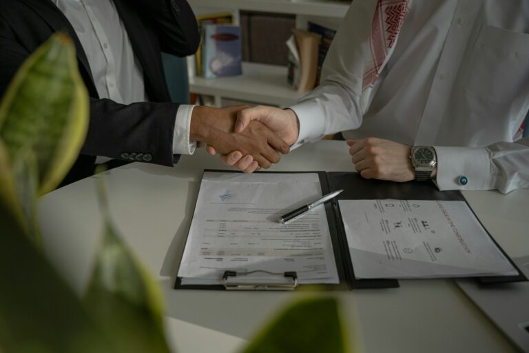 Two business professionals shaking hands over signed documents representing a completed business sale